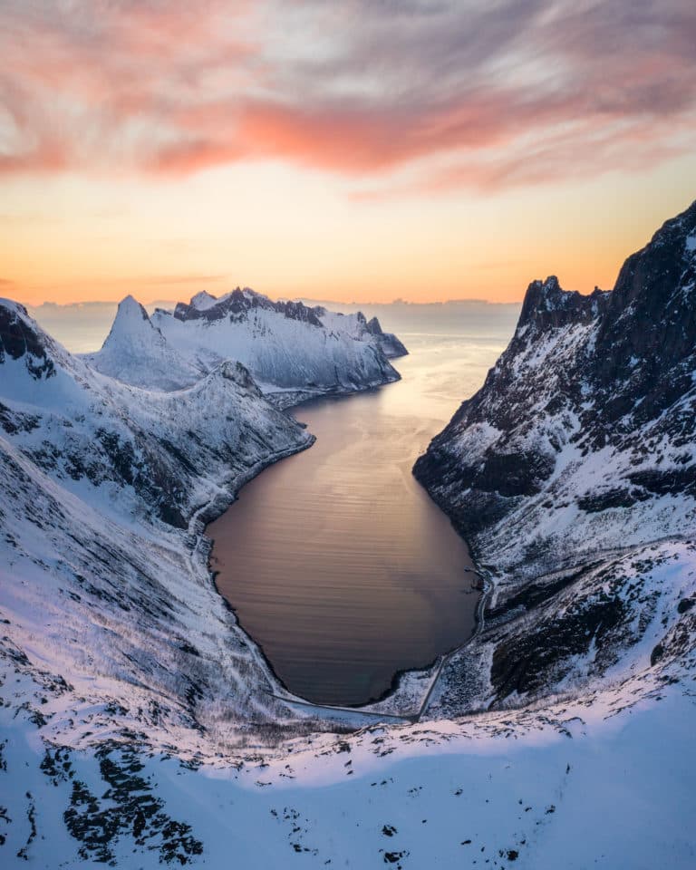 Aerial view of snow-covered Senja peaks framing a fjord inlet at sunset
