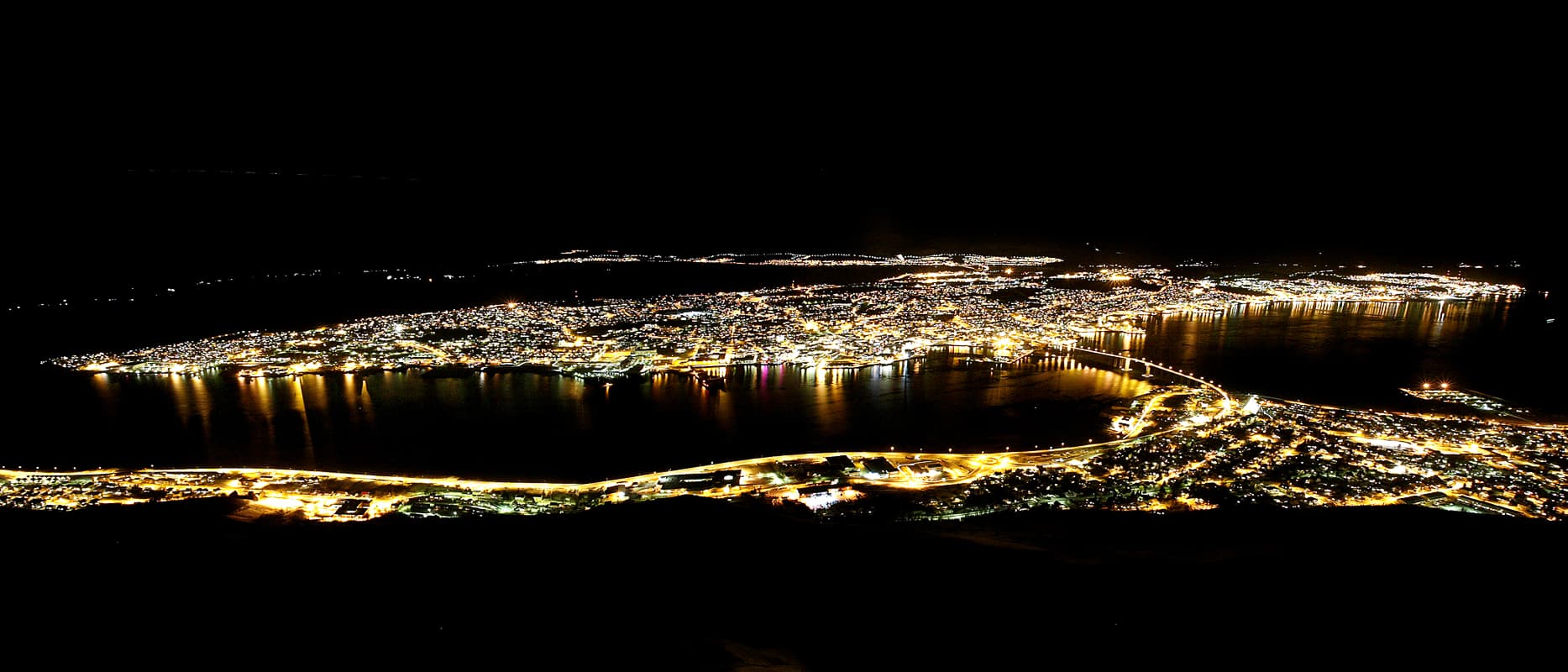 Tromsø at night seen from above, city lights and the Tromsø Bridge reflected in the strait