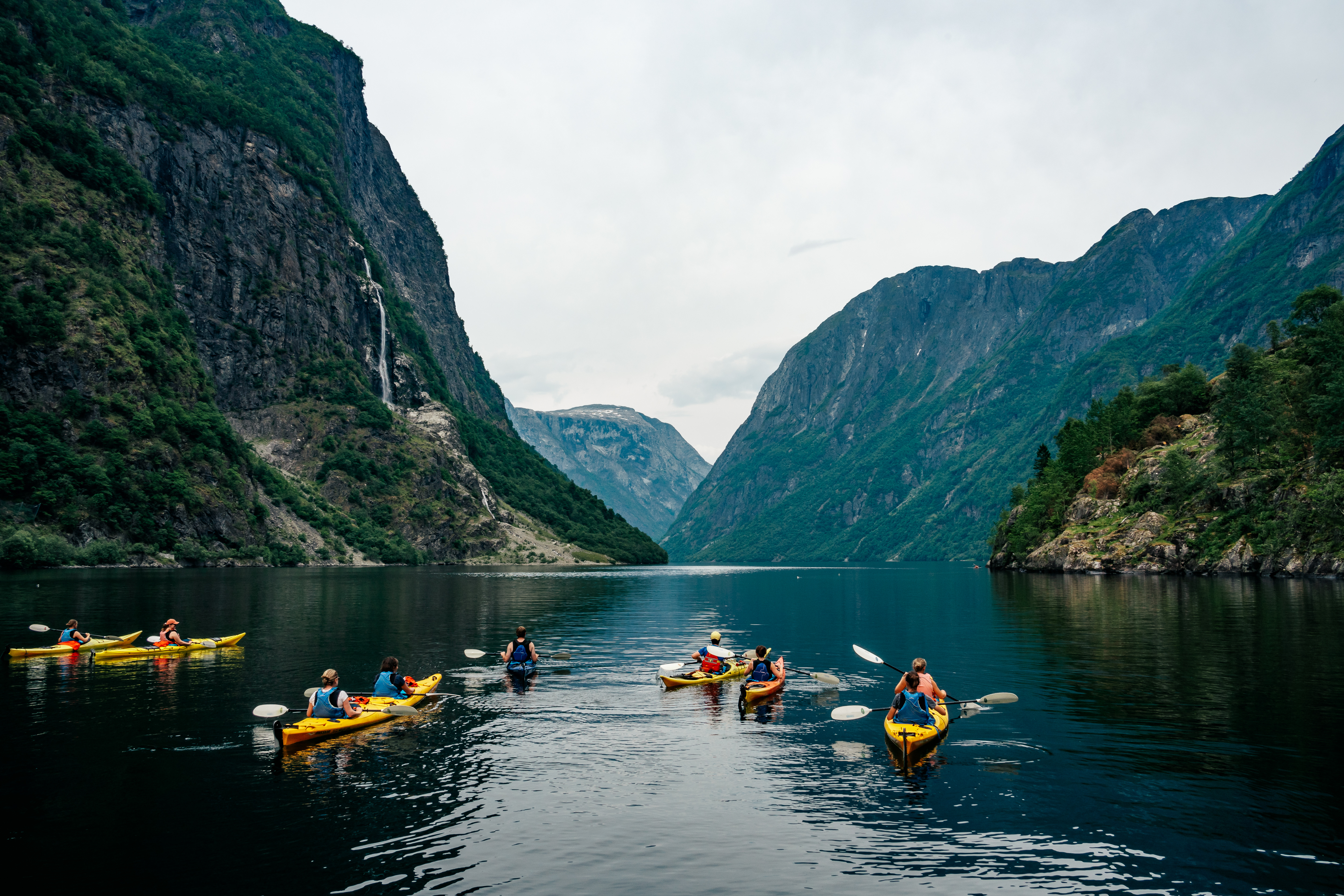 Guided kayakers paddling into Nærøyfjord from Gudvangen. Fjord walls close on both sides.
