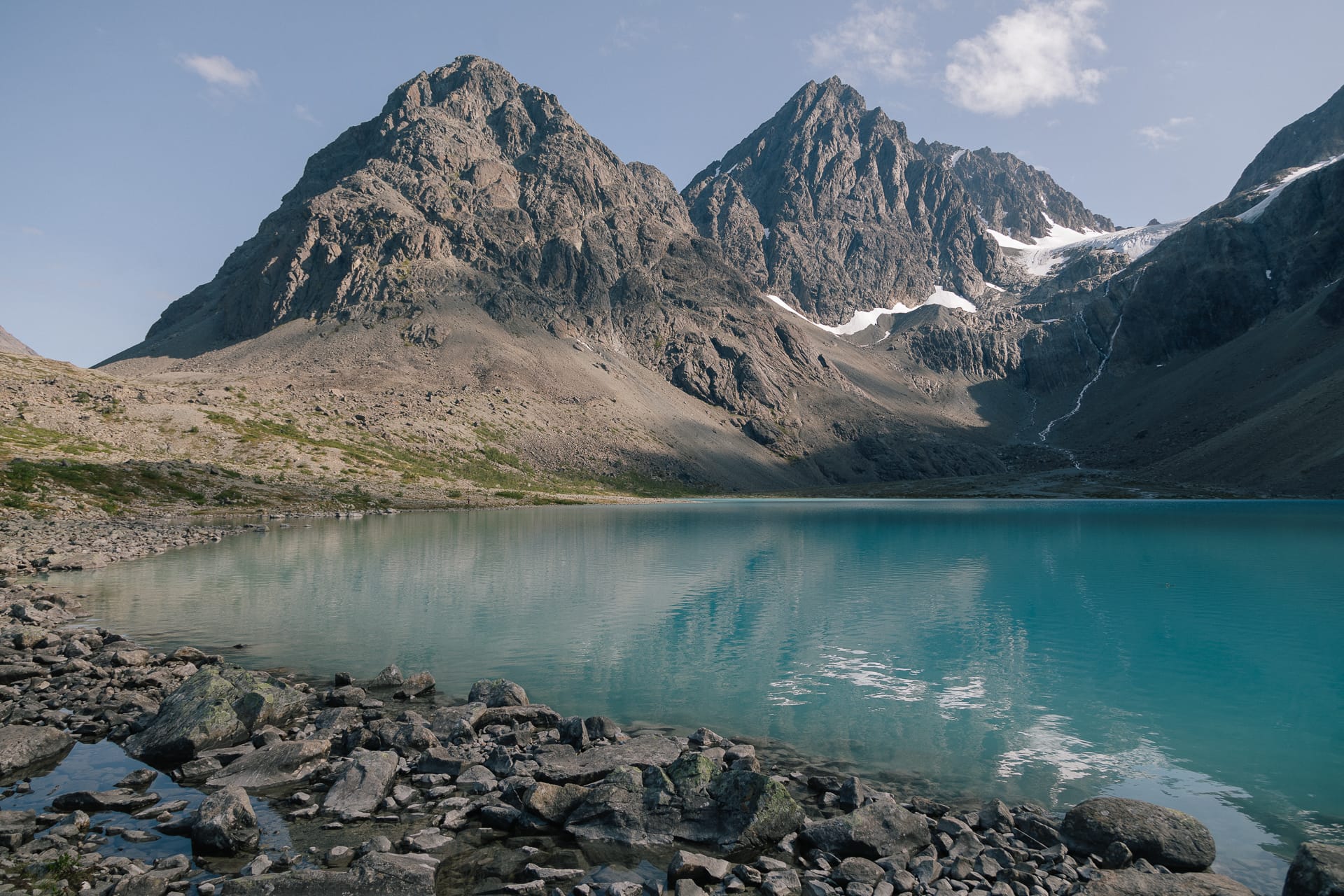 Turquoise water of Blåisvatnet below grey peaks and the Lenangsbreen glacier, with a boulder shore in the foreground