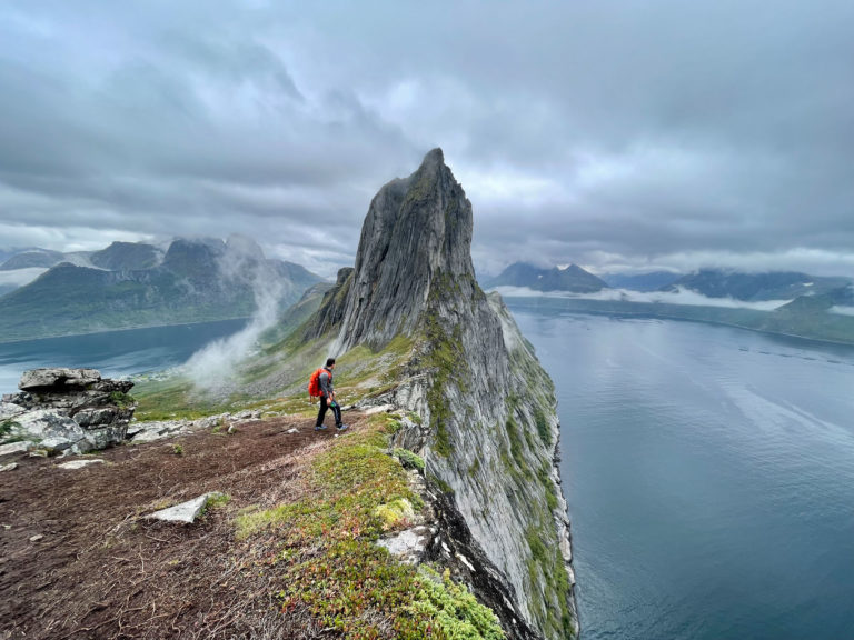 Hiker ascending Segla peak on Senja, steep exposed terrain with fjord 600 meters below