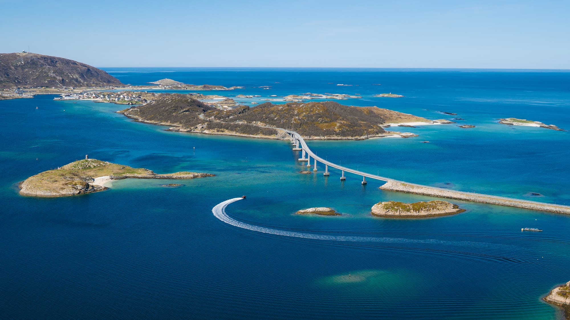 Sommarøy island and Kvaløya coastline under blue sky, white sand beach and turquoise shallow water with mountains rising on the mainland beyond